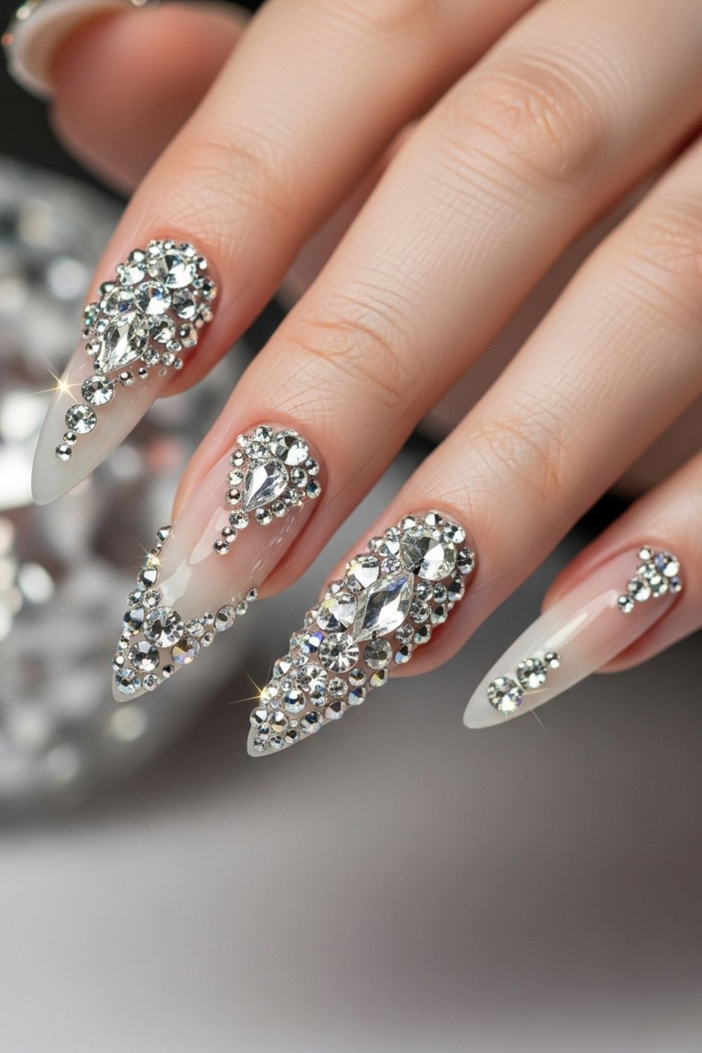 “Close-up of a straight hand with long stiletto luxury nails decorated with crystals, rhinestones, and shimmering details, elegant blurred nail salon background.”
