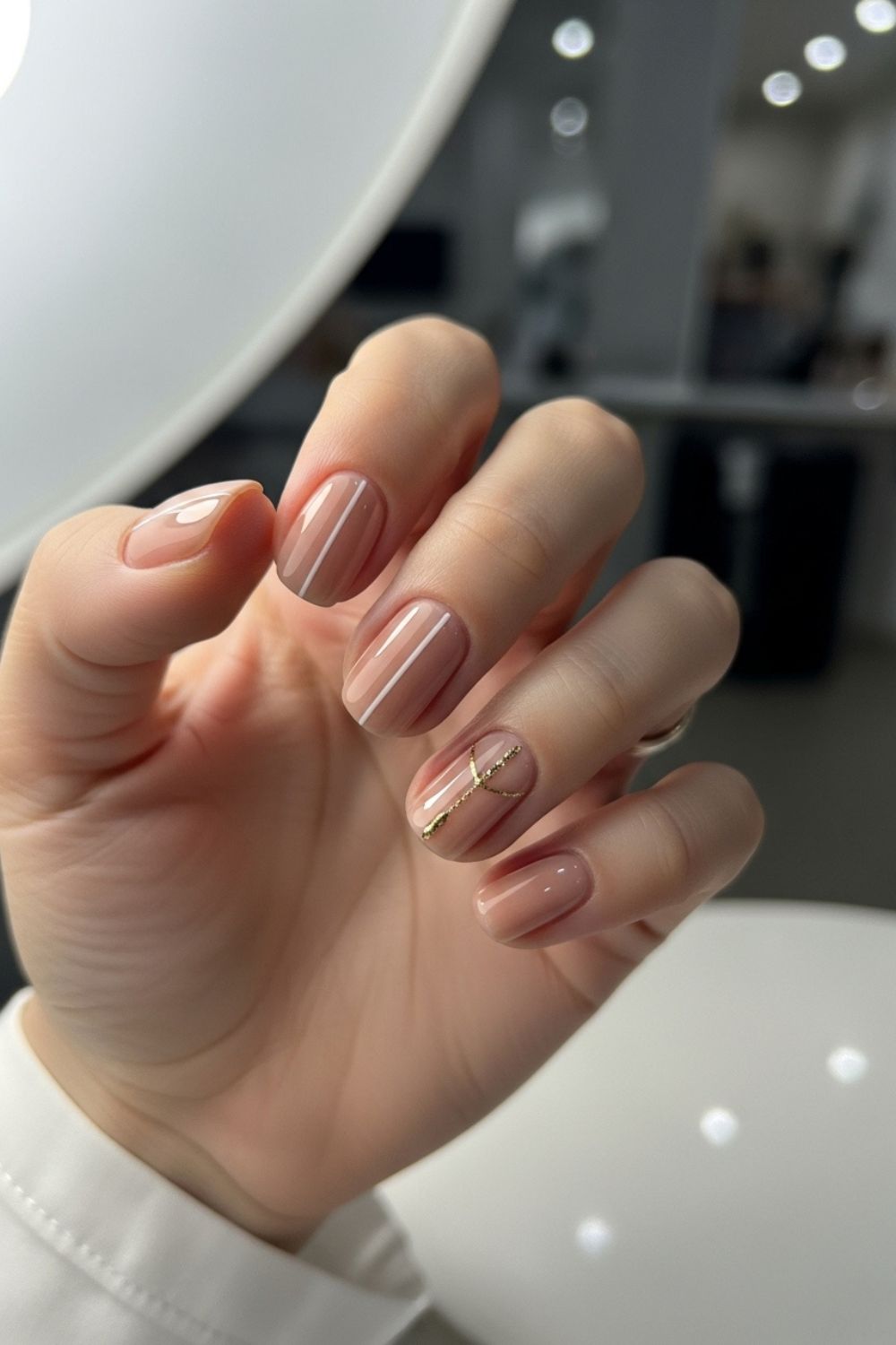 “Close-up of a straight flat hand with nude nails featuring minimal white lines and delicate gold accents, bright clean background softly blurred.”