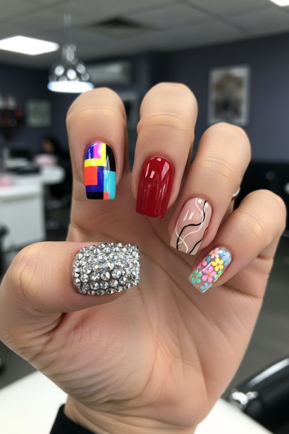 “Close-up of a straight flat hand showing different nail styles on each finger: bold acrylic, glossy gel, minimal nude art with fine lines, pastel floral seasonal, and crystal-studded luxury nail. Bright lighting with a softly blurred modern nail salon background.”